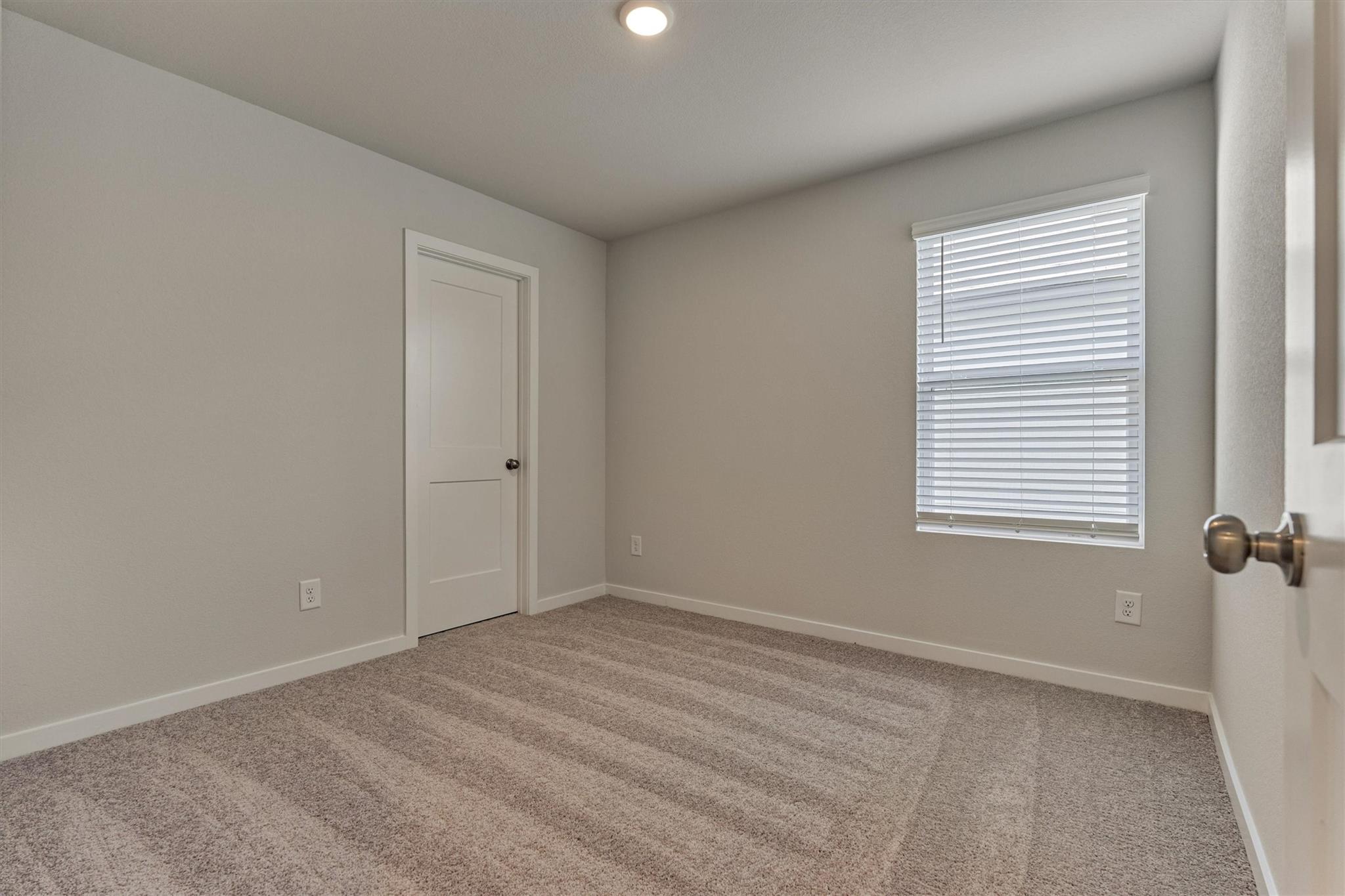 Empty bedroom with beige carpet and a window with white blinds.