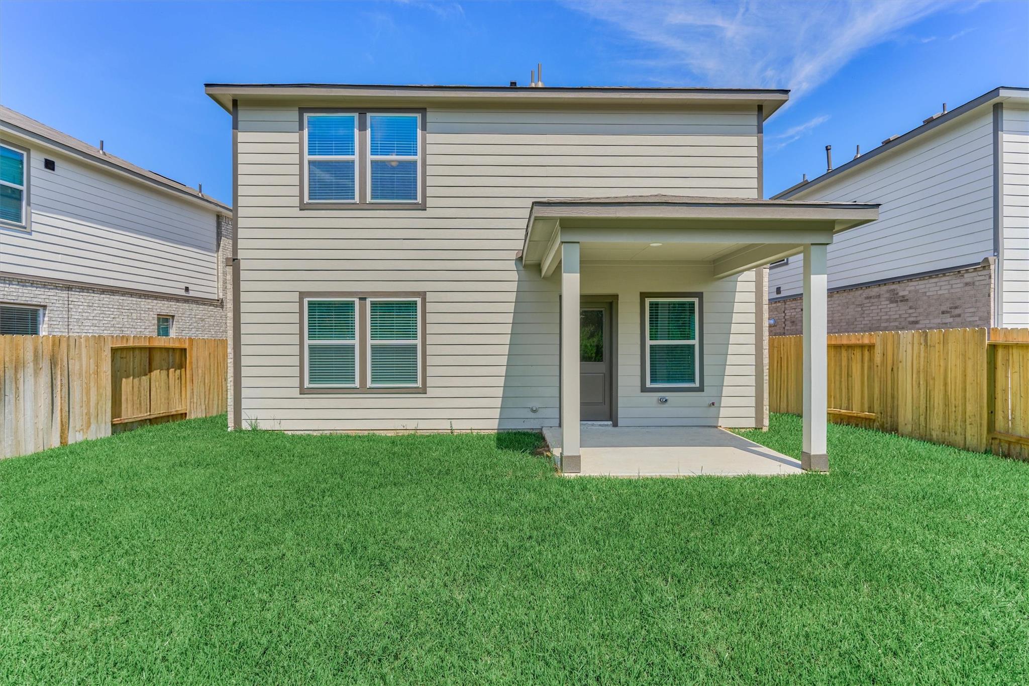 Two-story home with a covered rear patio and fenced, grassy backyard.