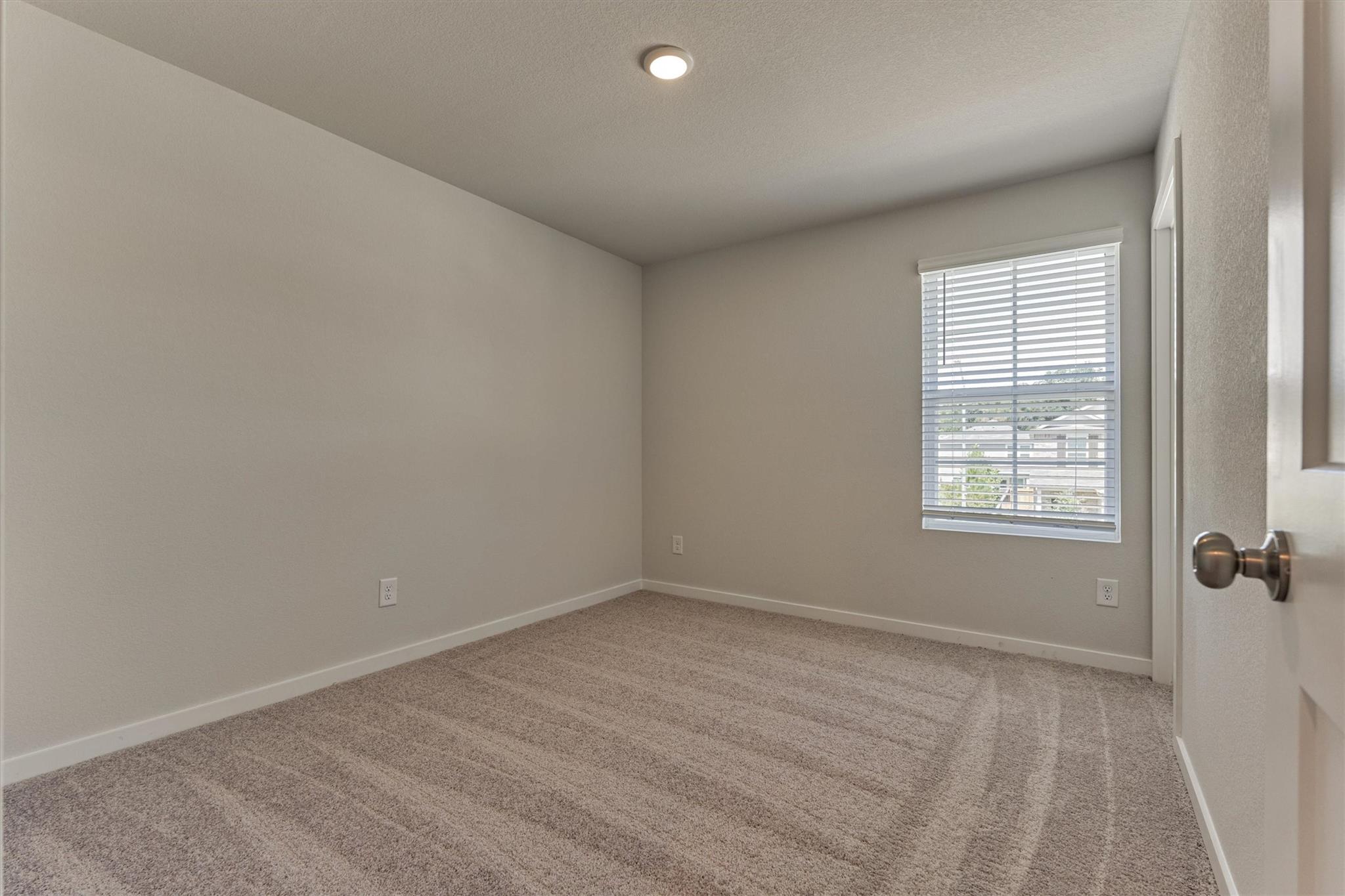Empty bedroom with beige carpet and a window with white blinds.