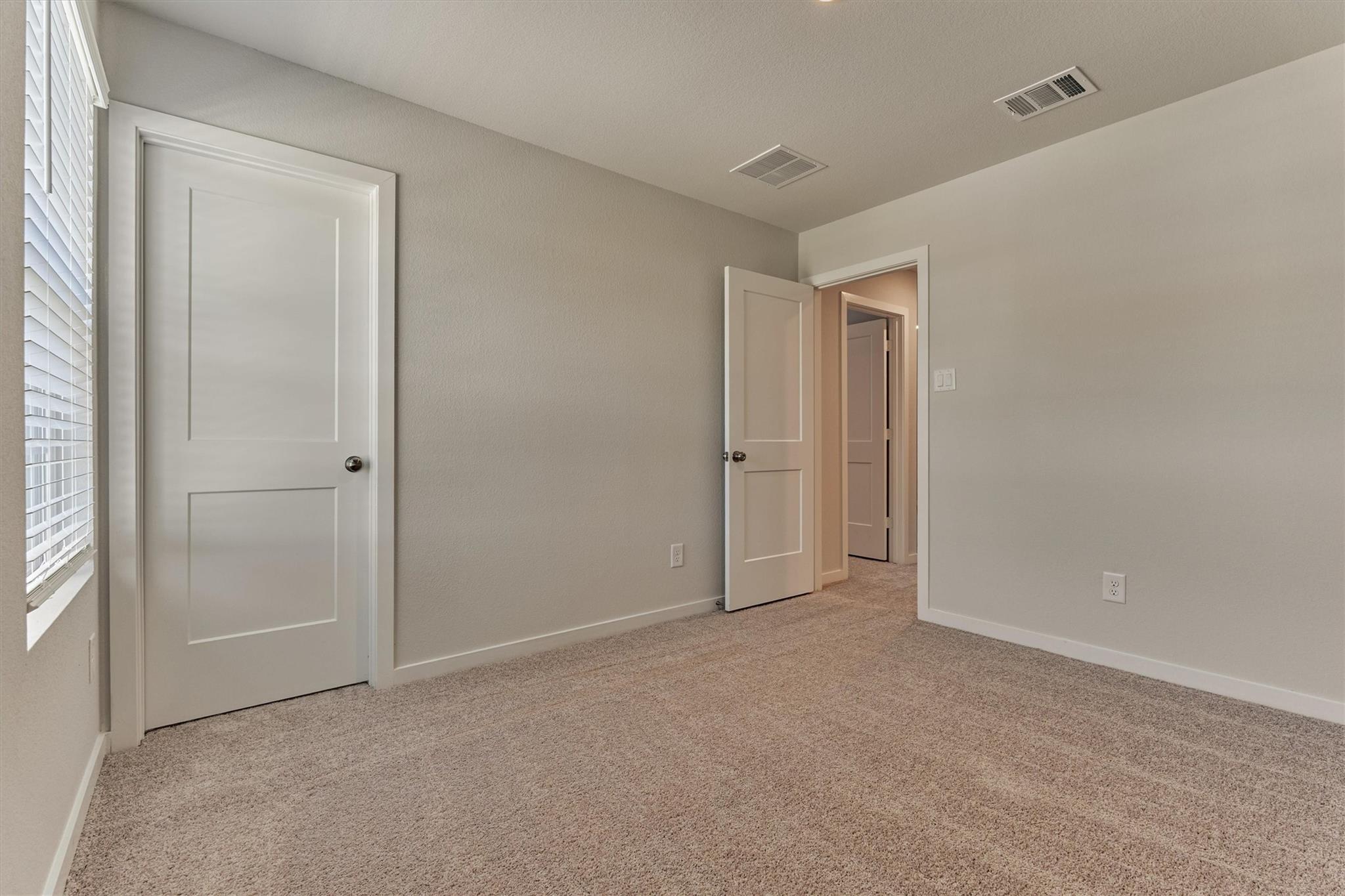 Empty carpeted bedroom with a window and open doors to the hallway.