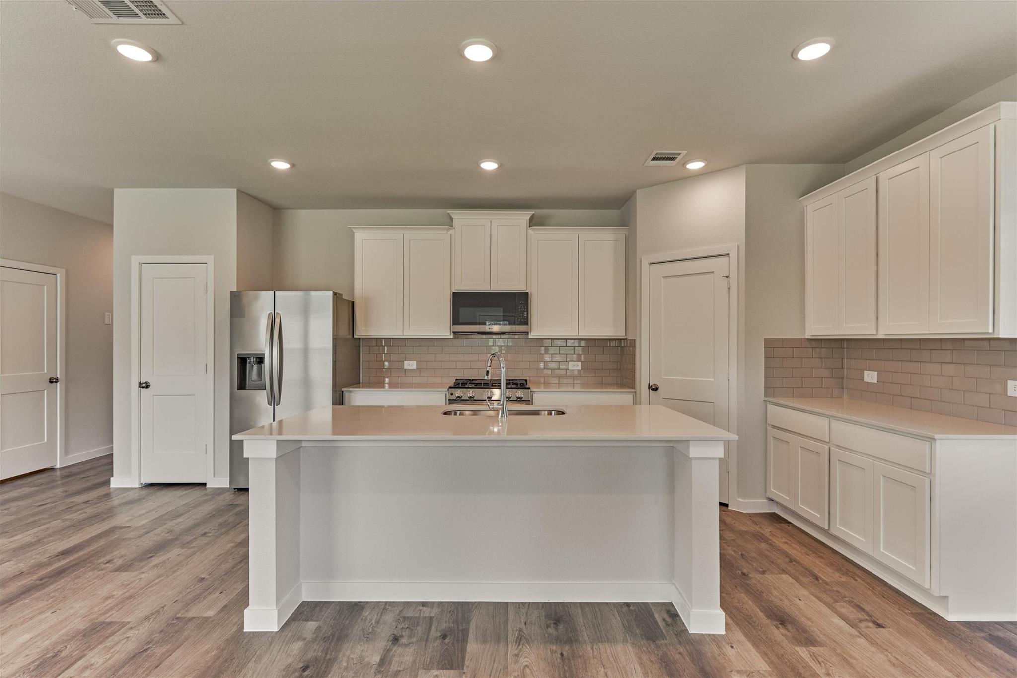 Kitchen with a large white island, stainless steel appliances, and taupe subway-tile backsplash.