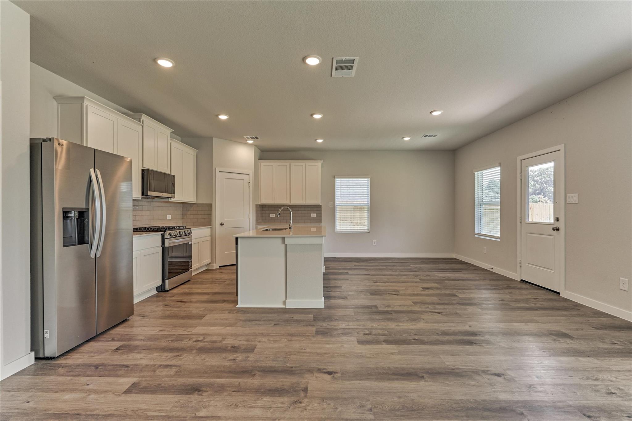 Open kitchen and living area with white cabinets, stainless steel appliances, and wood-look flooring.
