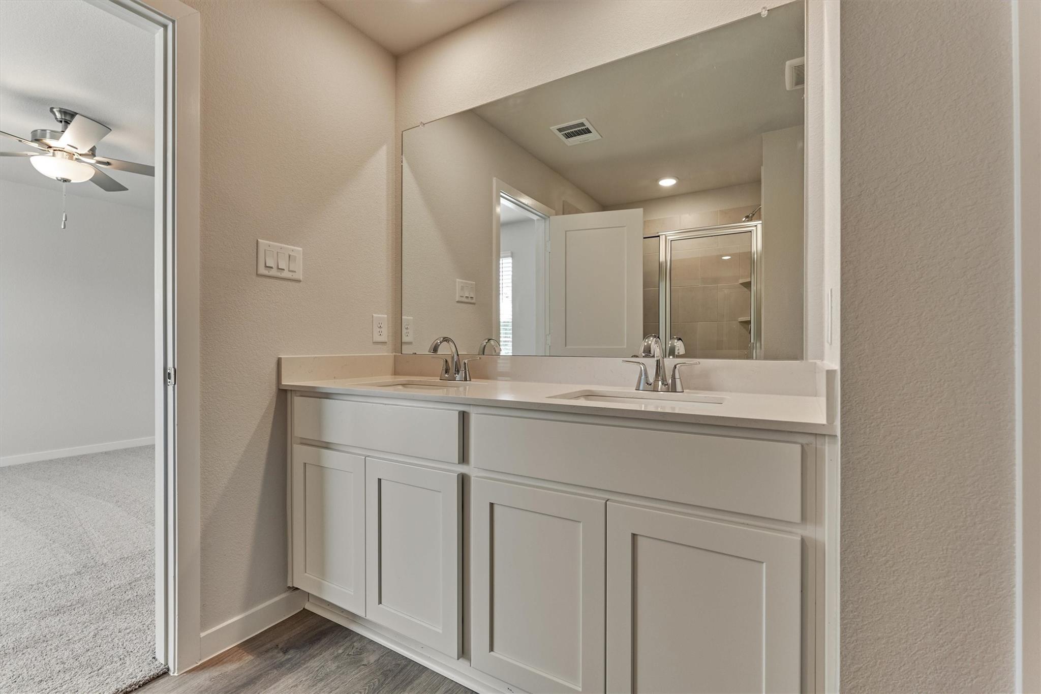 Bathroom with a white double-sink vanity and large mirror, with a glass shower reflected behind it.