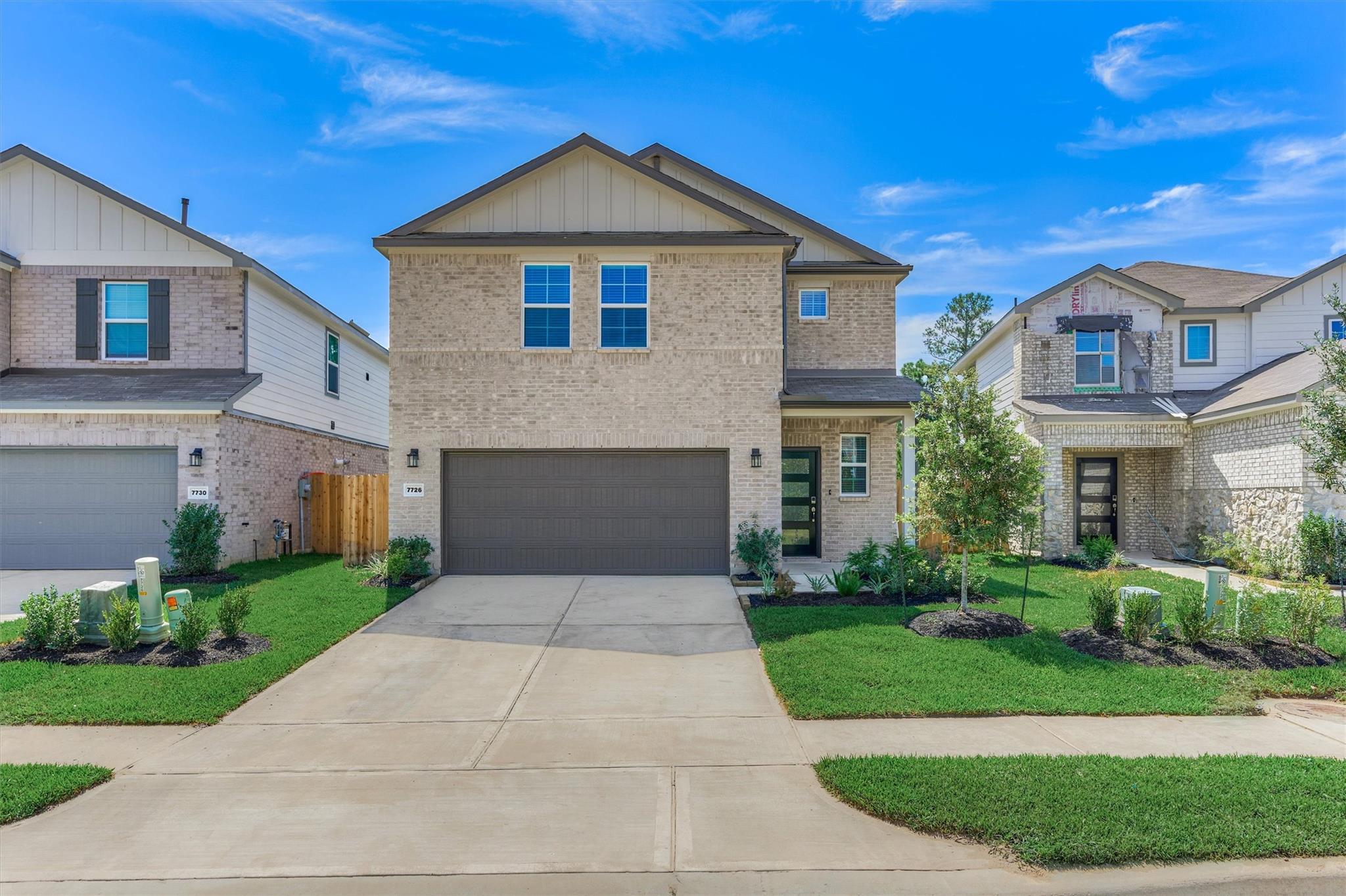 Two-story tan brick home with a dark double garage and landscaped front lawn.