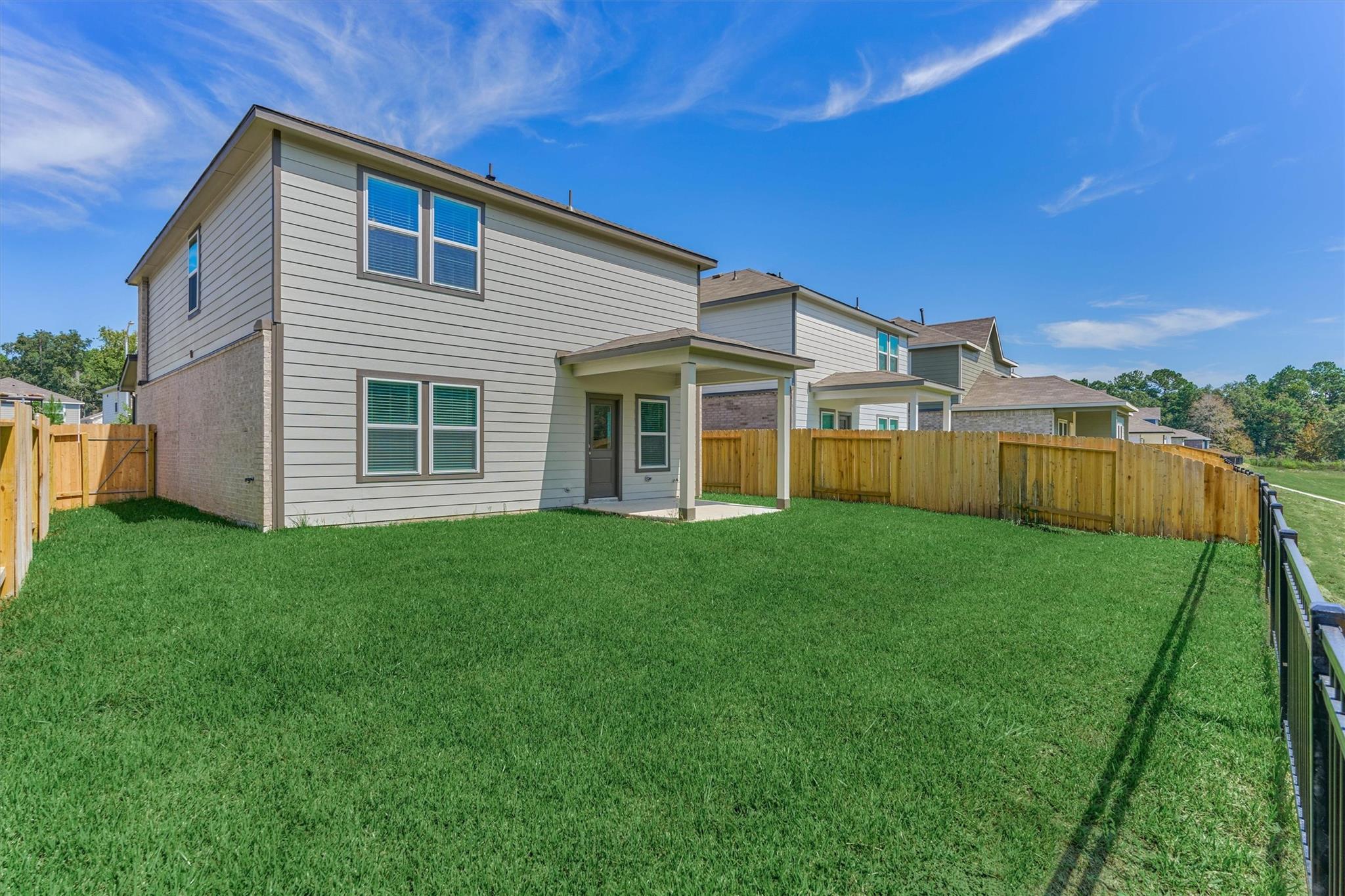 Two-story home overlooking a broad fenced lawn, with a small covered patio.