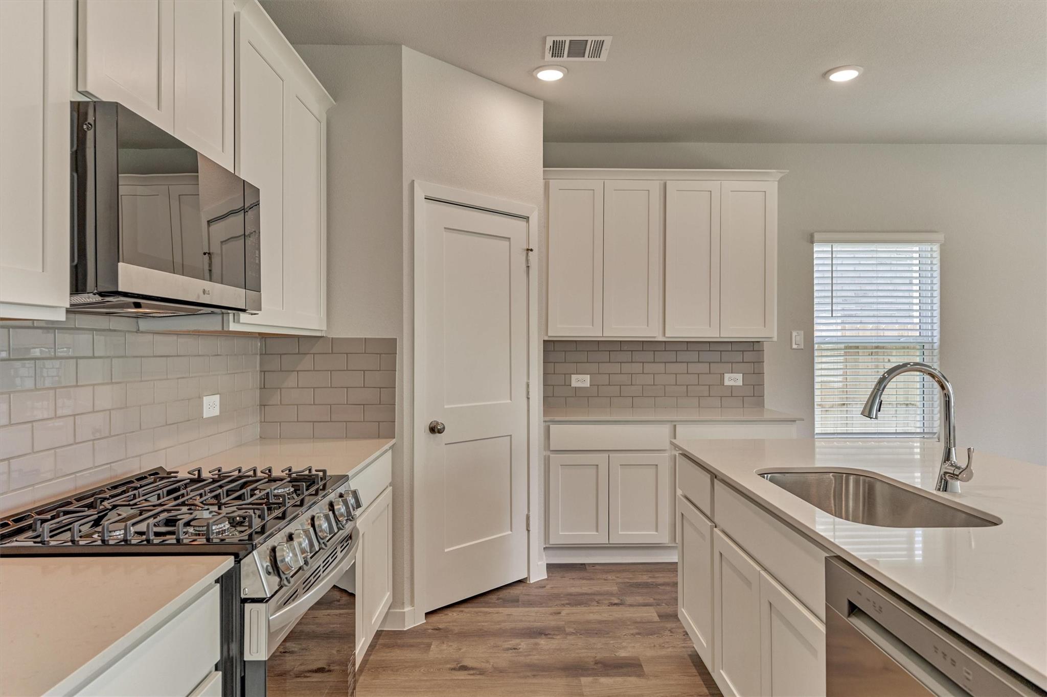 Kitchen with white shaker cabinets, subway tile backsplash, gas range, and a large island sink.