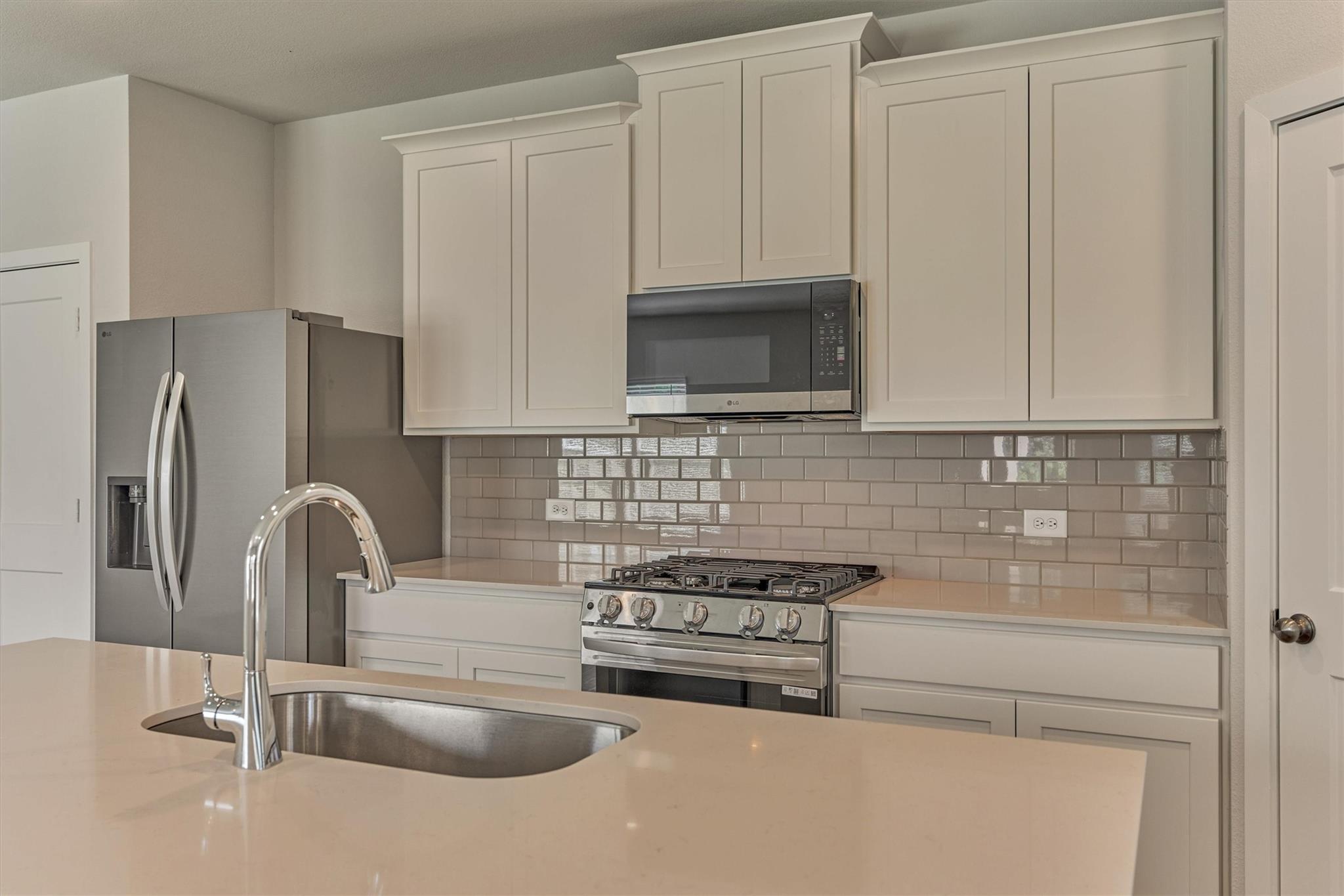 Kitchen with white shaker cabinets, stainless appliances, gray tile backsplash, and a large island sink.