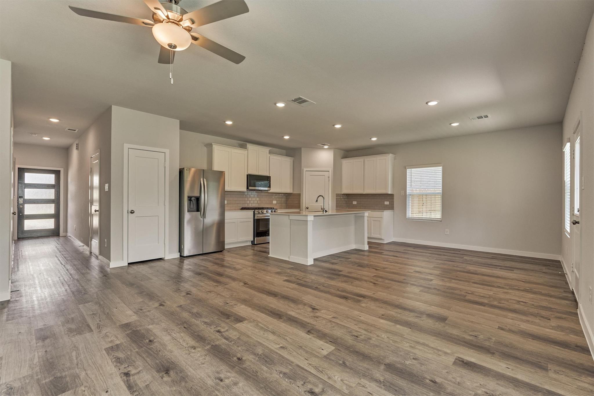 Open-plan kitchen and living area with a white island, stainless steel appliances, and wood-look flooring.