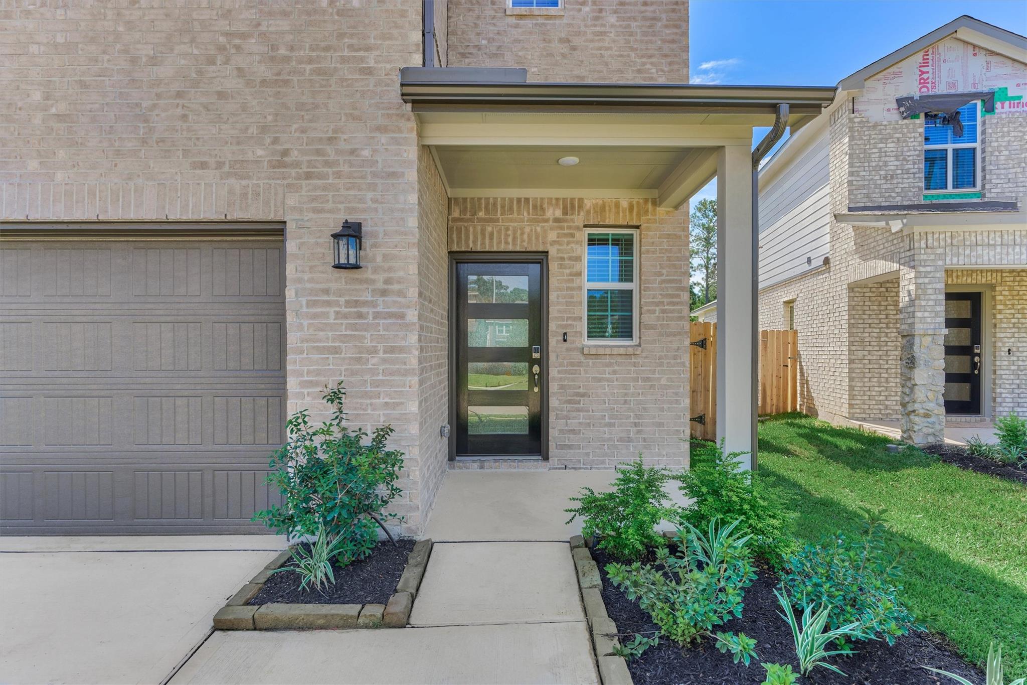 Brick home’s covered front entry beside the garage, with a landscaped walkway and dark glass-paneled door.