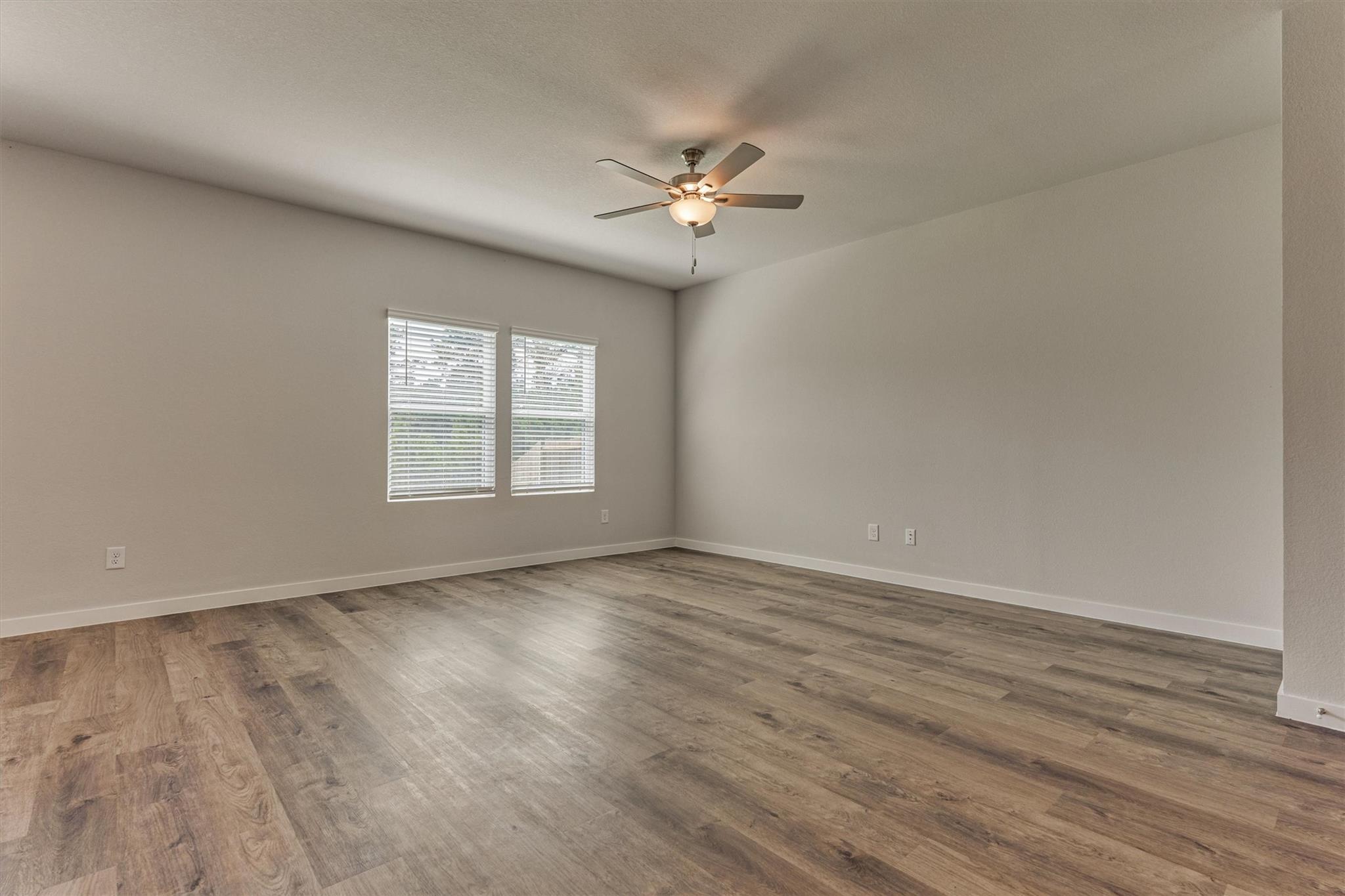 Empty room with wood-look plank flooring, two blinded windows, and a lit ceiling fan.