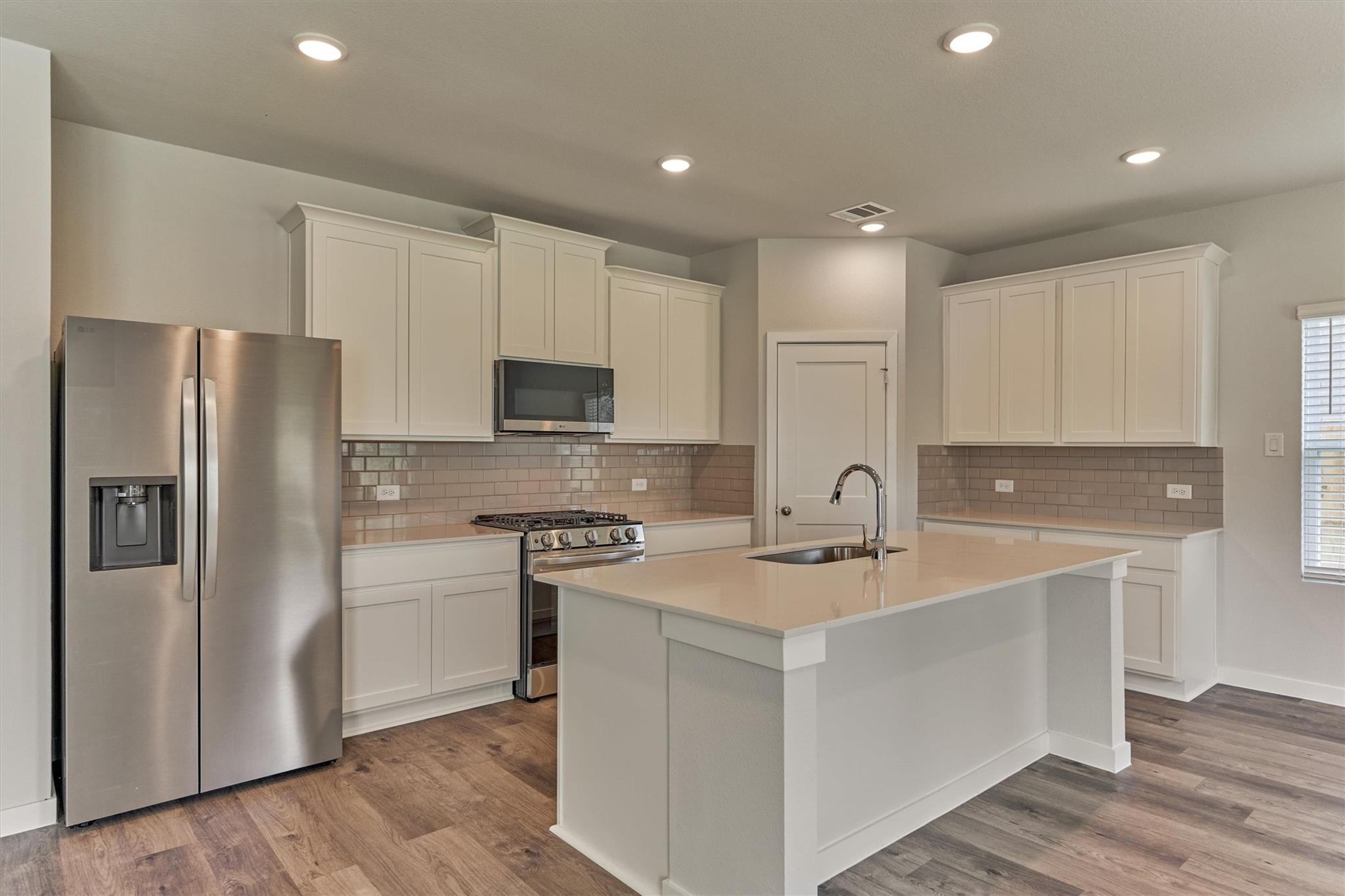Kitchen with white cabinets, stainless steel appliances, and a large island with sink.