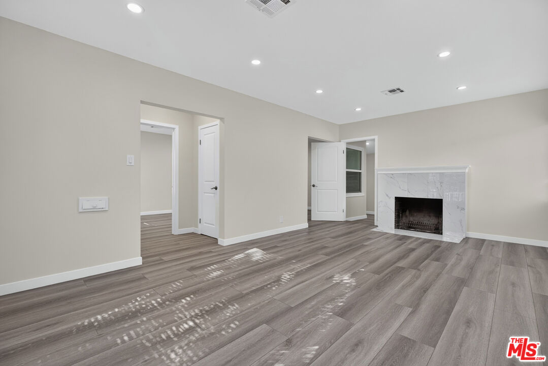 Vacant living room with gray plank flooring and a white marble-look fireplace.