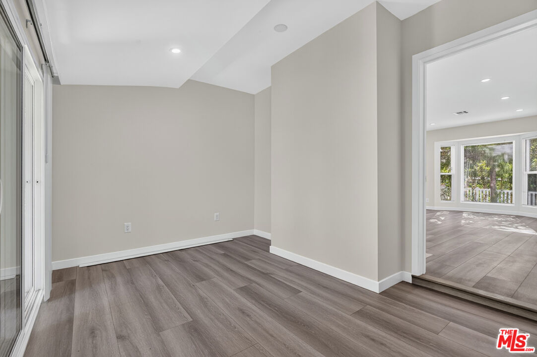 Empty room with gray plank flooring and sliding glass doors, opening to a bright windowed room.