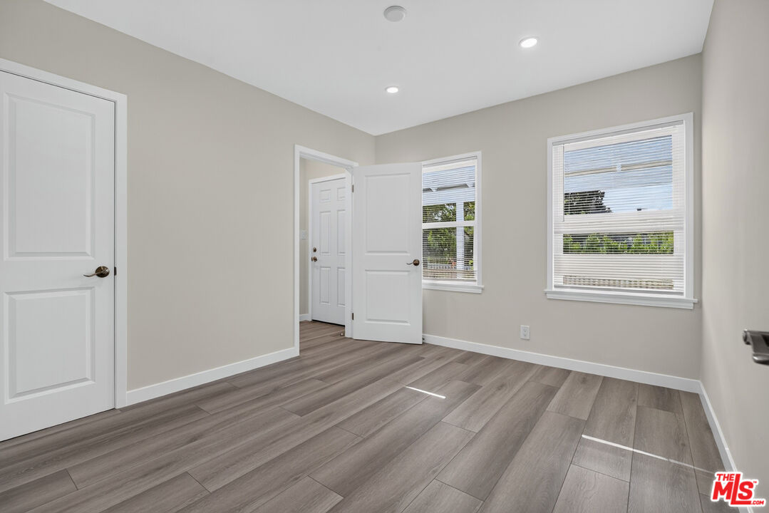 Empty room with gray plank flooring, recessed lights, and two windows with blinds.