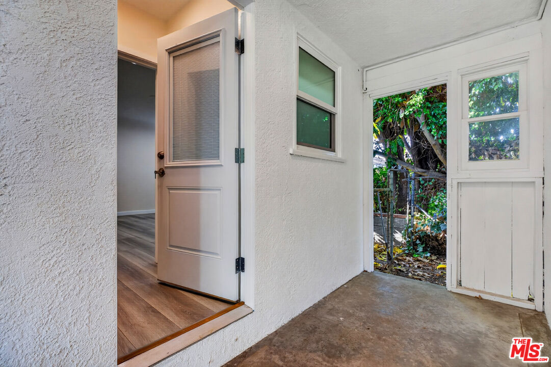Covered entry porch with an open door and windows overlooking a leafy yard.