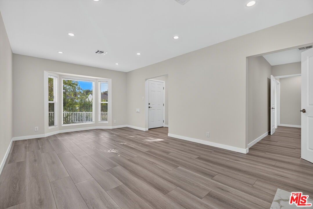 Vacant room with plank flooring and a large bay window overlooking trees.
