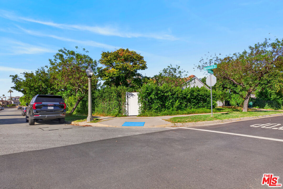 Street-corner view of a house partly screened by dense hedges and trees, with a garage and Dartmouth Road sign.