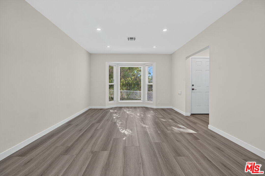 Vacant room with gray wood-look flooring and a bay window overlooking trees and a white railing.