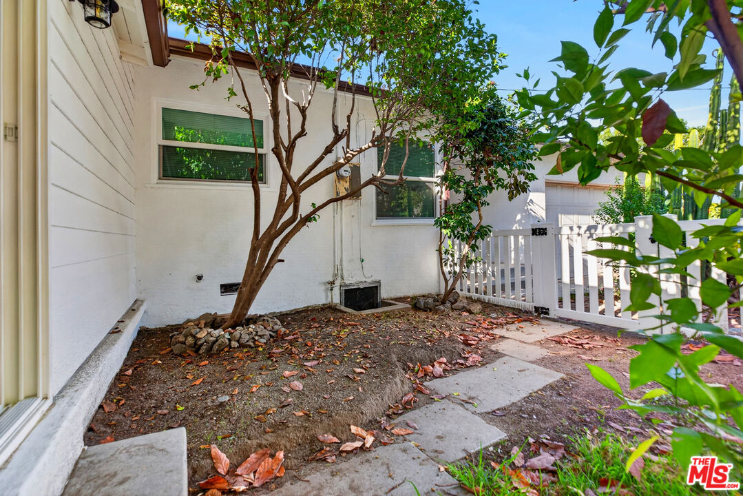 White home's side yard with a concrete path, small trees, and a white picket fence.