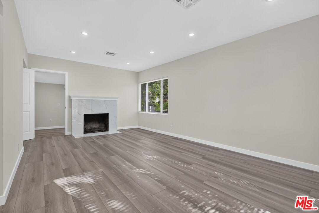 Vacant living room with gray wood-look floors, a marble fireplace, and a window with blinds.