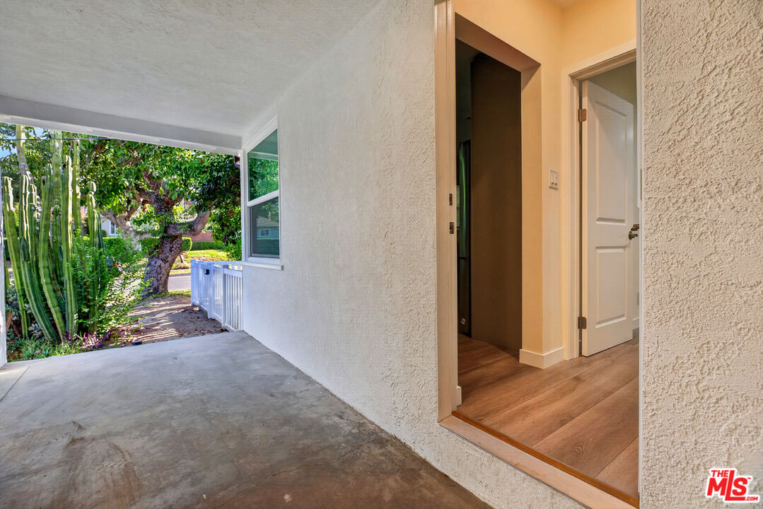 Covered concrete entry beside a stucco wall, with a garden and tall cacti outside.