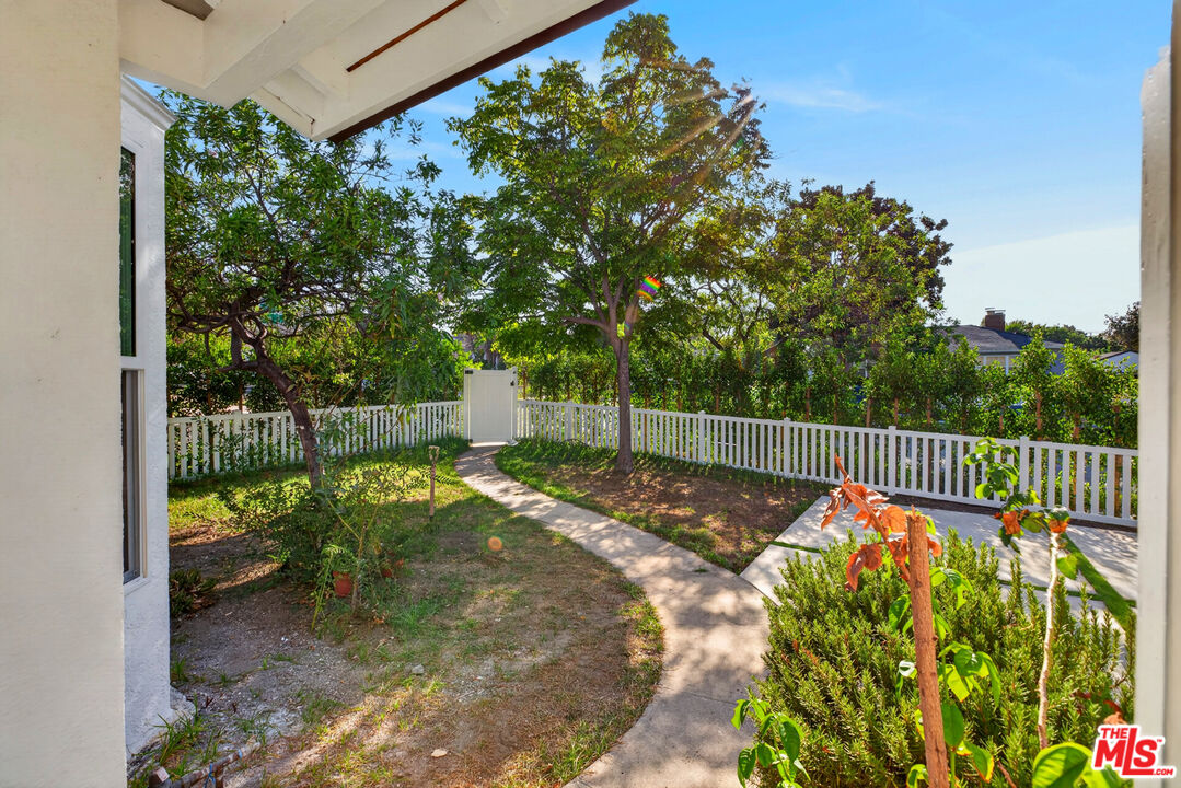 Backyard with a curved walkway, white picket fence, mature trees, and a small patio.