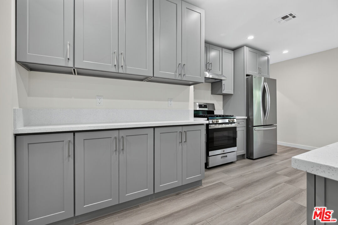 Kitchen with gray cabinets, white counters, stainless steel appliances, and gray wood-look flooring.