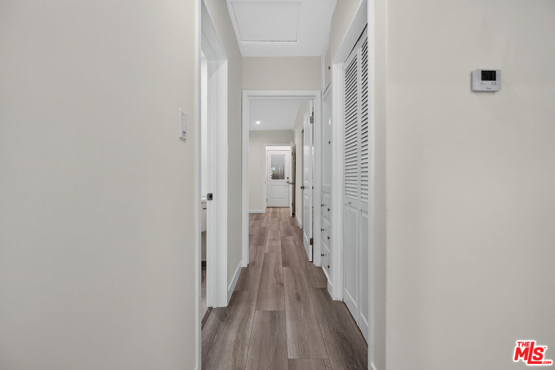 Empty hallway with plank flooring, louvered closet doors, and a door at the far end.