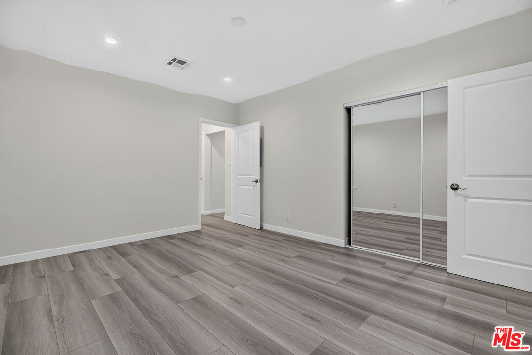 Vacant bedroom with gray plank flooring and mirrored sliding closet doors.