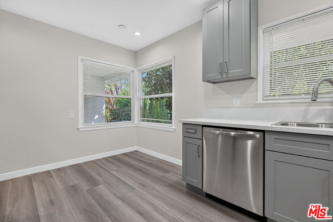 Kitchen with gray cabinets, stainless steel dishwasher, corner windows, and gray wood-look flooring.