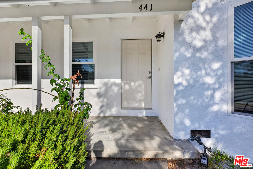 Covered front entrance with the house number 441, a white paneled door, and shrubs.