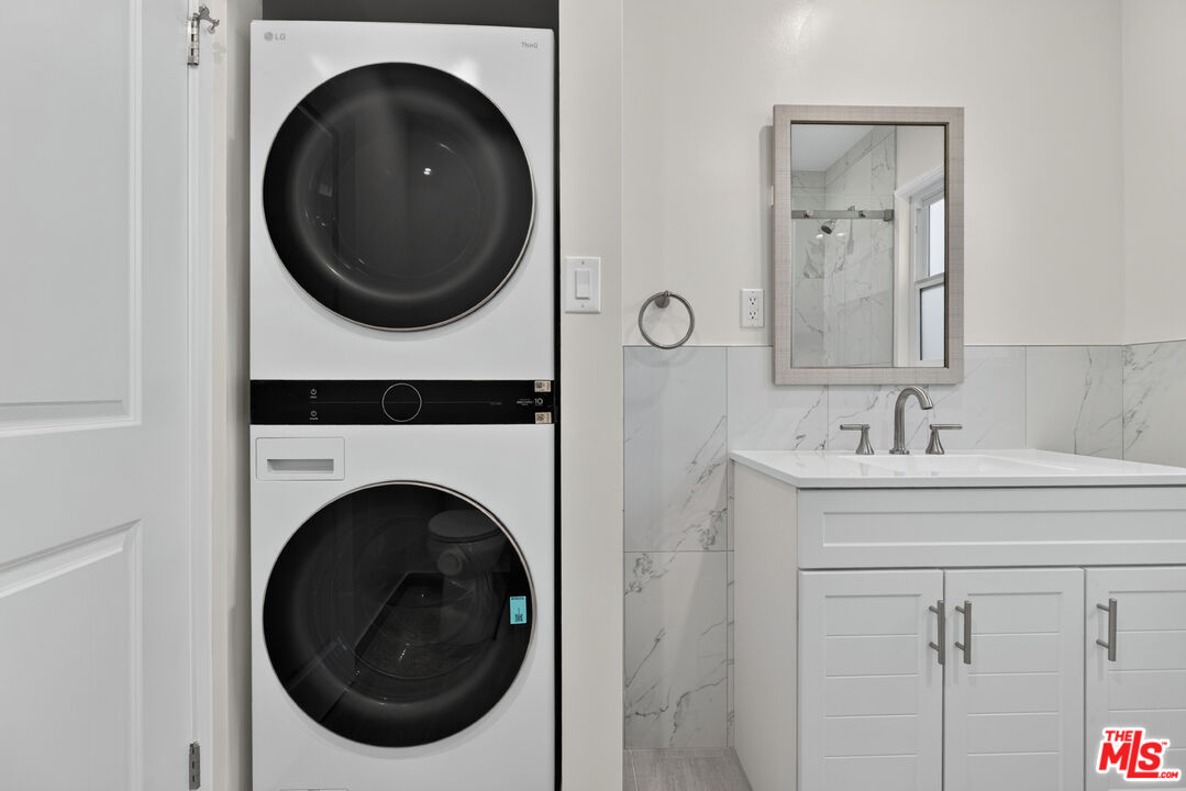 Bathroom with stacked washer and dryer beside a white vanity and marble-look tile.