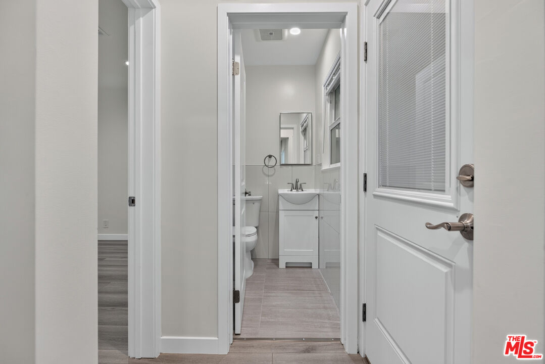 Bathroom with a white vanity and mirror, toilet, tiled floor, and window with blinds.
