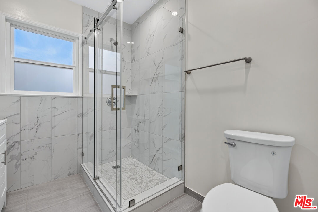 Bathroom with a glass-enclosed shower, marble-look tile, mosaic floor, and window.