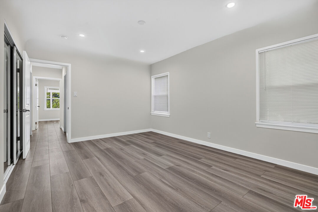 Empty room with gray plank flooring, recessed lights, and windows with closed blinds.