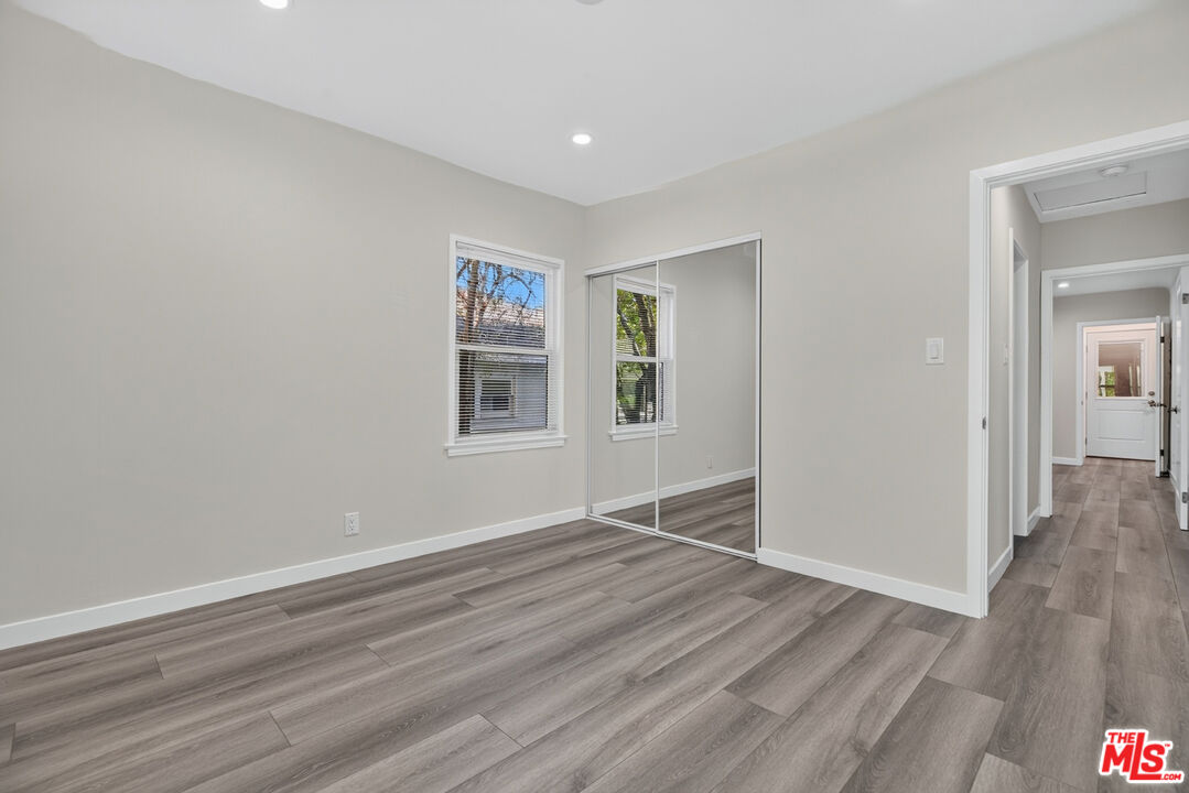 Empty bedroom with mirrored closet doors, gray plank flooring, and two windows.