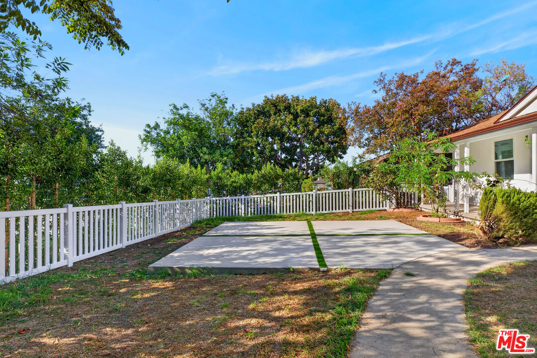Fenced yard with a broad concrete patio, white picket fence, and mature trees.