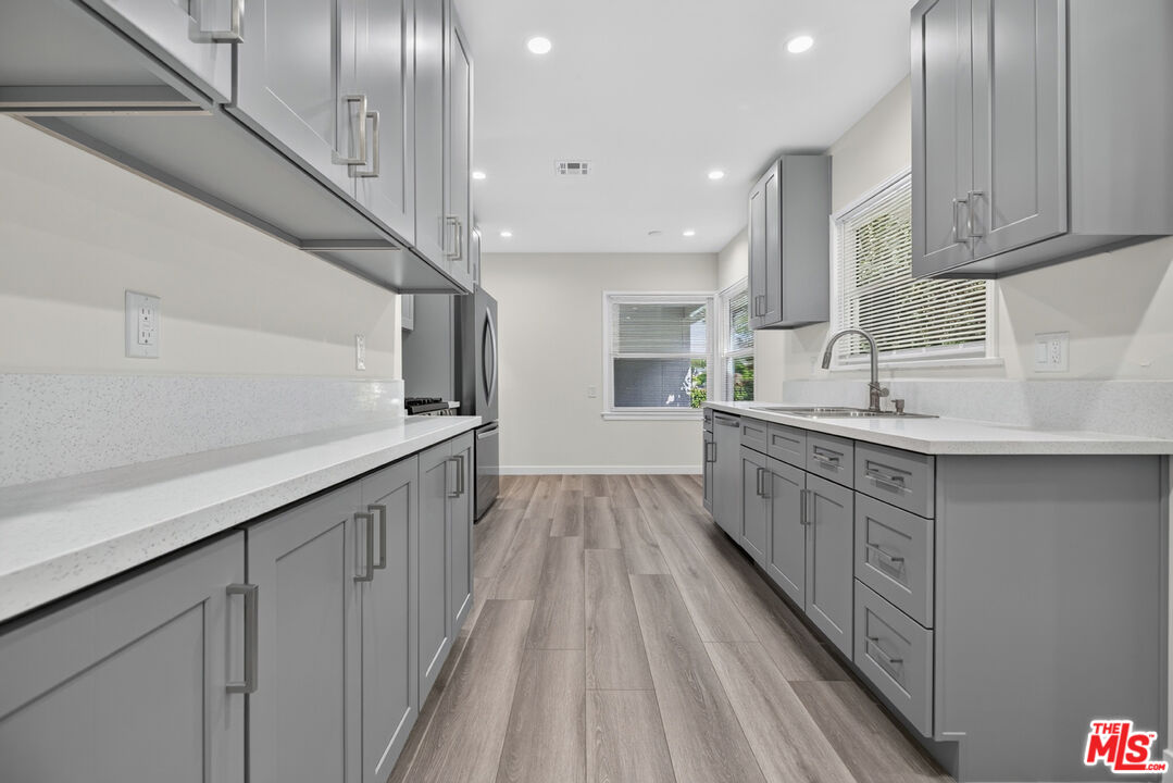 Kitchen with gray cabinets, white countertops, stainless steel refrigerator, and wood-look flooring.