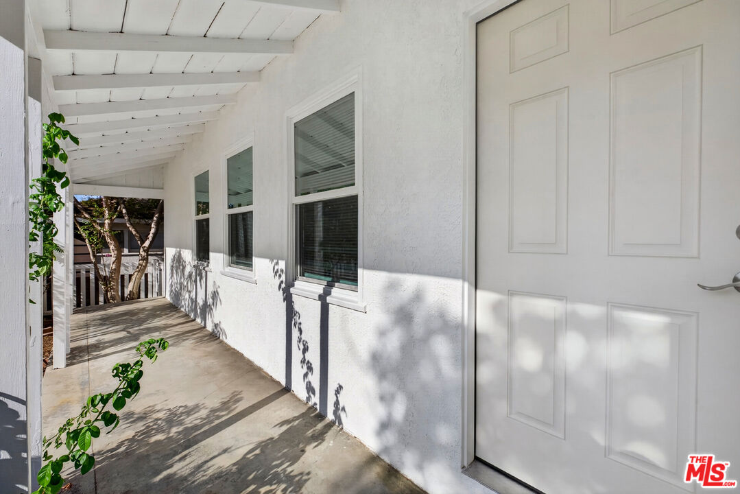 Covered entry walkway with a white paneled door, windows, and exposed ceiling beams.