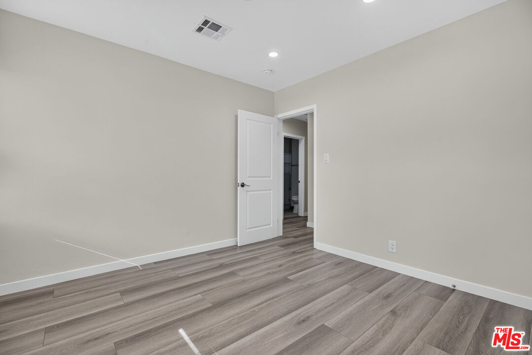 Empty bedroom with gray plank flooring and an open door to an adjacent bathroom.
