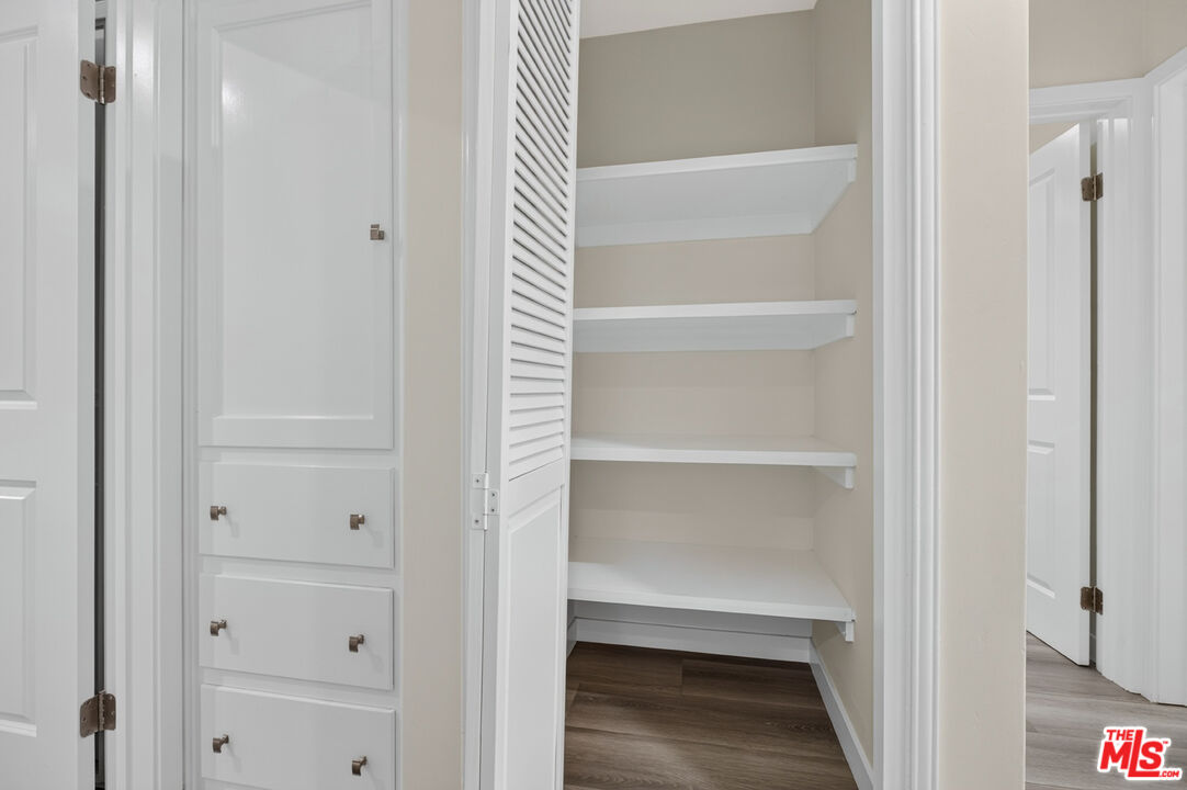 Walk-in closet with white shelves, a louvered door, and built-in drawers.