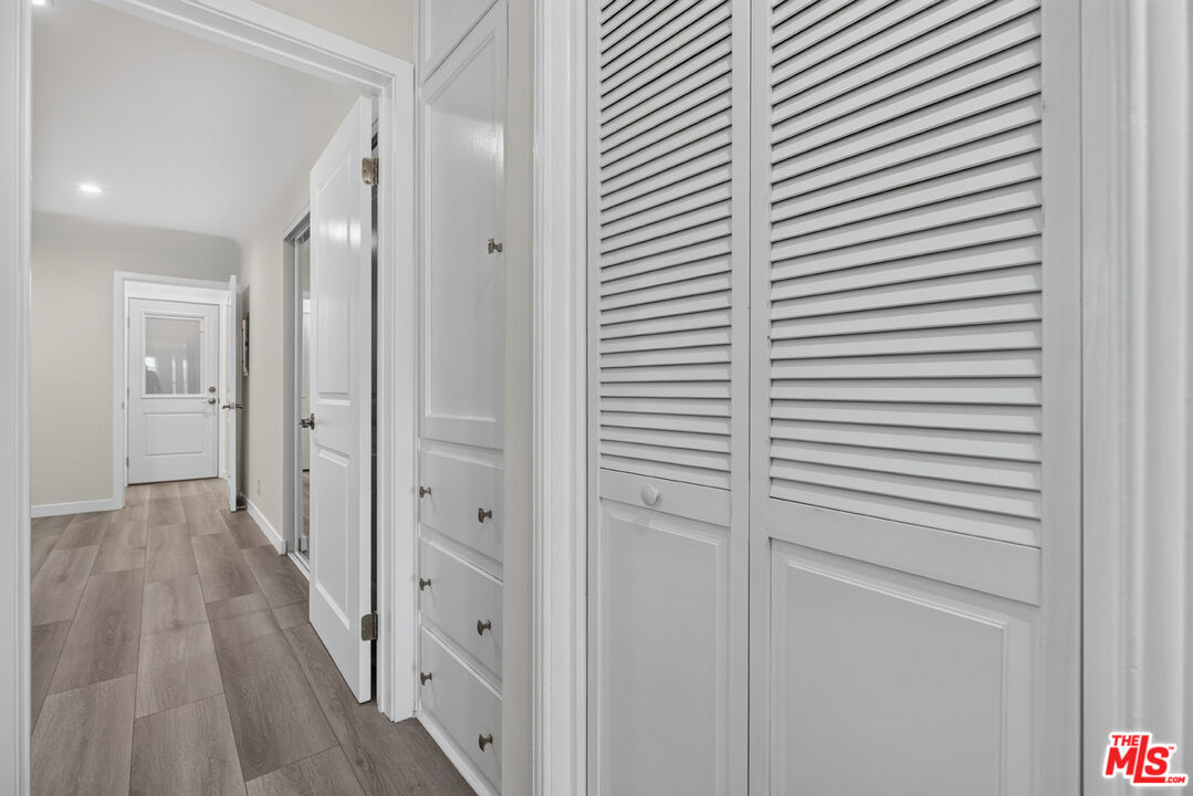 Hallway with white louvered closet doors, built-in drawers, and gray wood-look flooring.