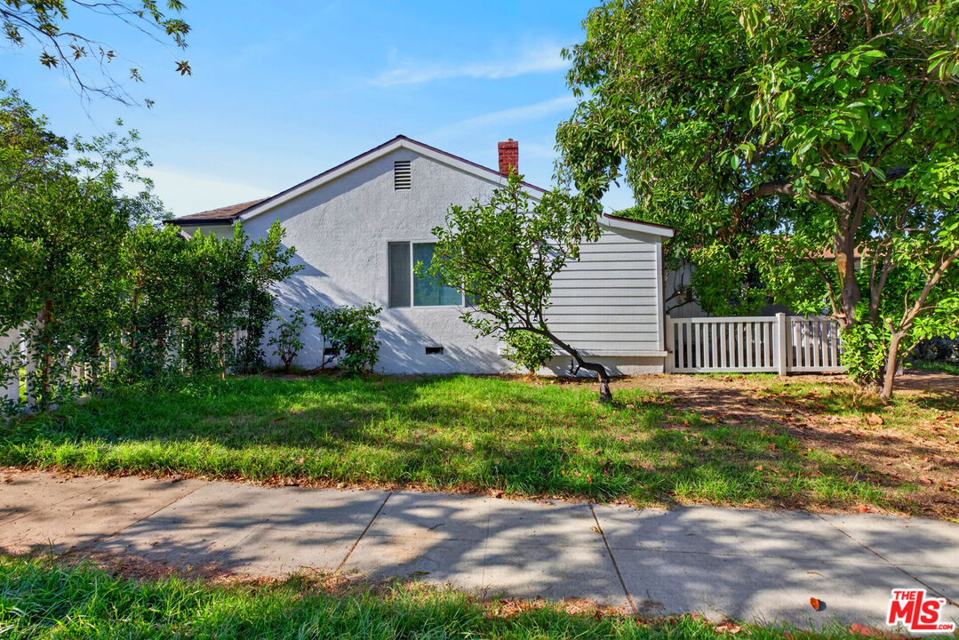 House exterior with light siding, a small raised deck, lawn, and mature trees.