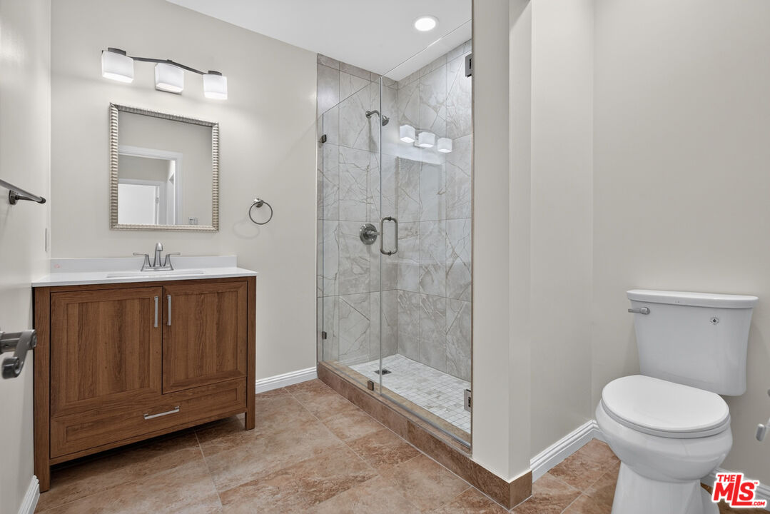 Bathroom with a wood vanity, glass-enclosed marble-look shower, and brown tile floor.