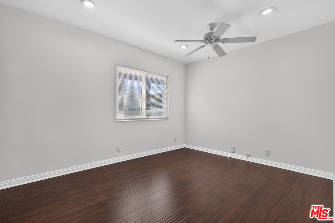 Vacant room with dark wood-look flooring, a window with blinds, and a ceiling fan.
