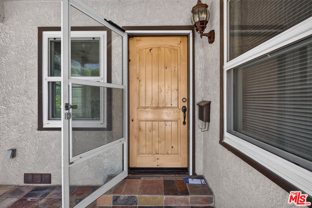 Front entrance with a light wood paneled door, open screen door, and tiled porch.