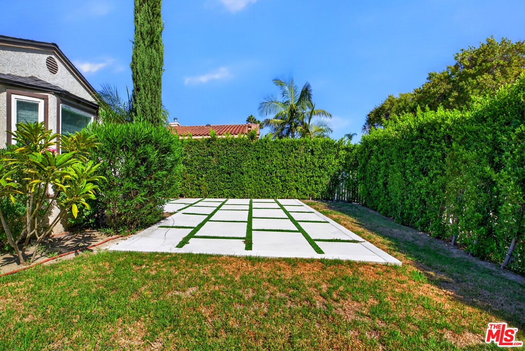 Landscaped backyard with a white paver patio, lawn, and tall privacy hedges.
