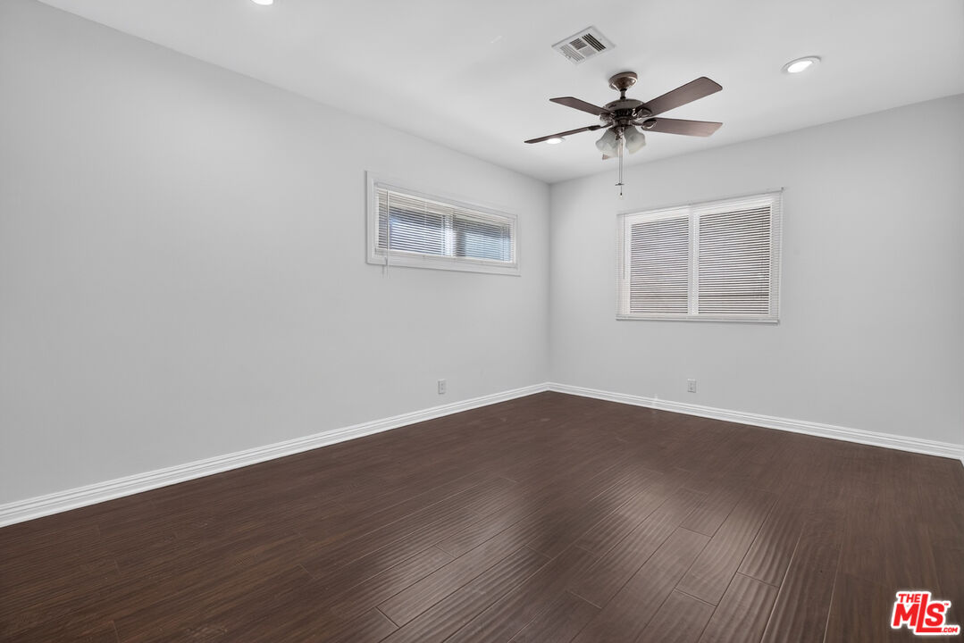 Empty bedroom with dark plank flooring, two curtained windows, and a ceiling fan.