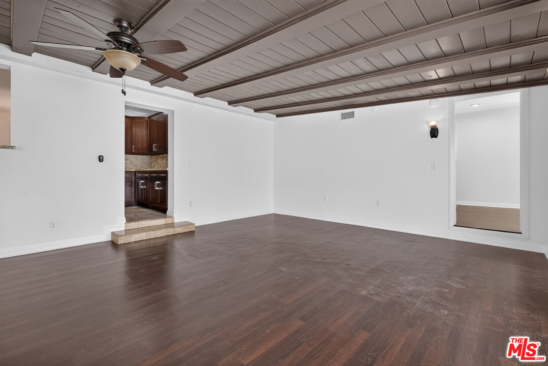 Empty living room with dark wood floors, a plank ceiling, and a ceiling fan.