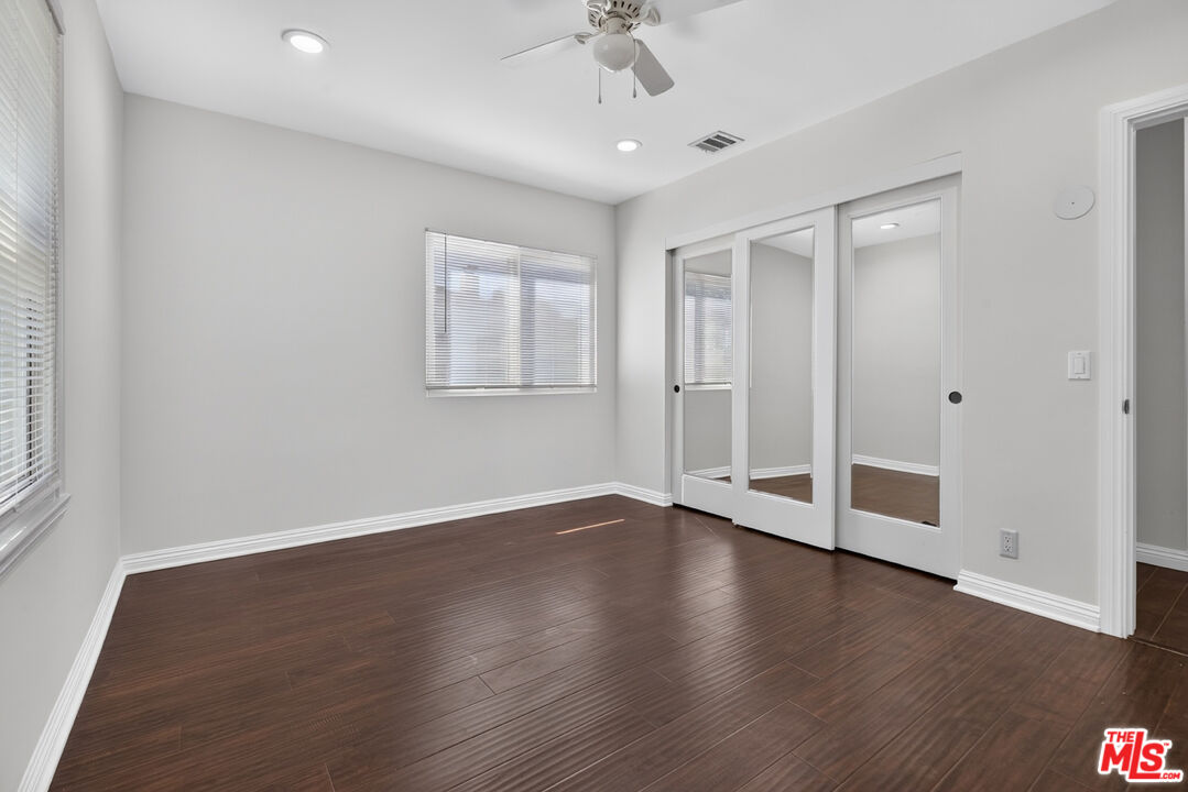 Empty bedroom with dark flooring, mirrored closet doors, window blinds, and a ceiling fan.